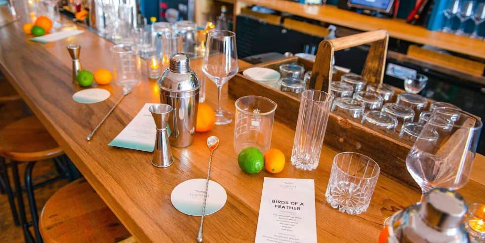 Photo displaying a cocktail shaker, measurer, limes, lemons, and oranges.